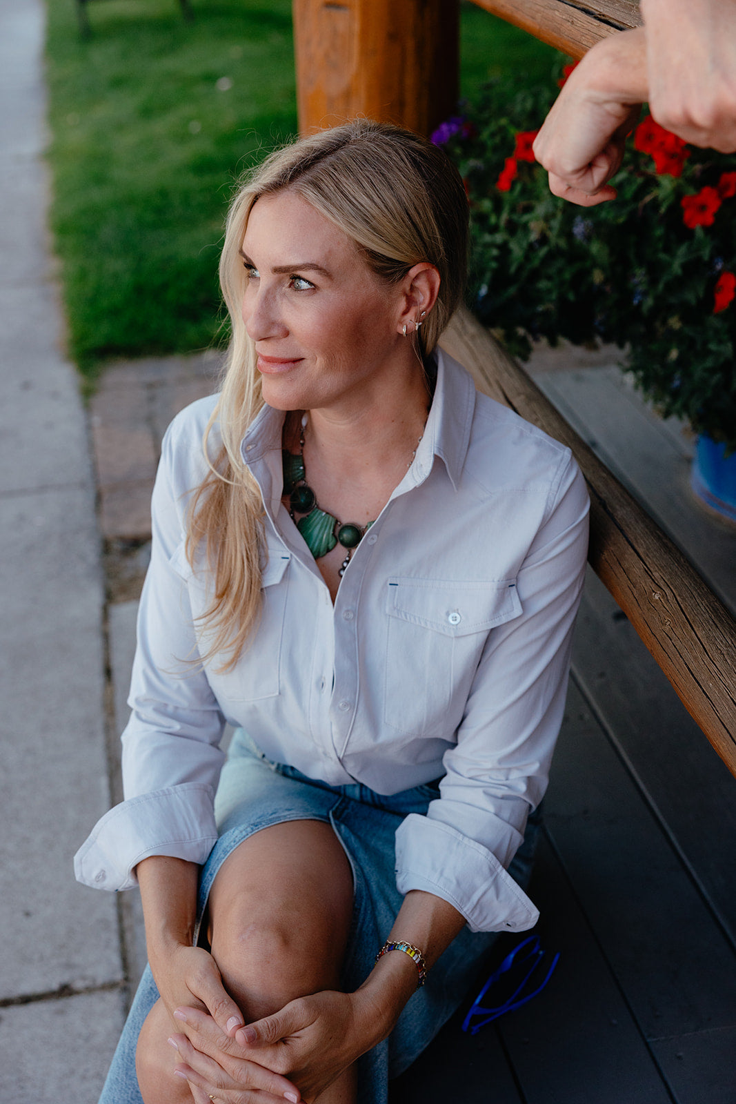 Woman sitting on a bench with flowers and greenery in the background wearing soca button down