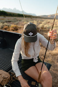 Person sitting in a truck bed with mountains in the background wearing a soča hat
