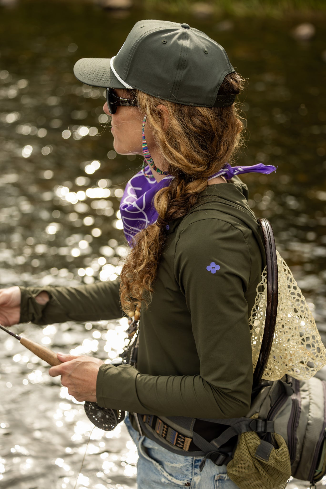 Woman fishing by a body of water wearing a green sun shirt and cap.