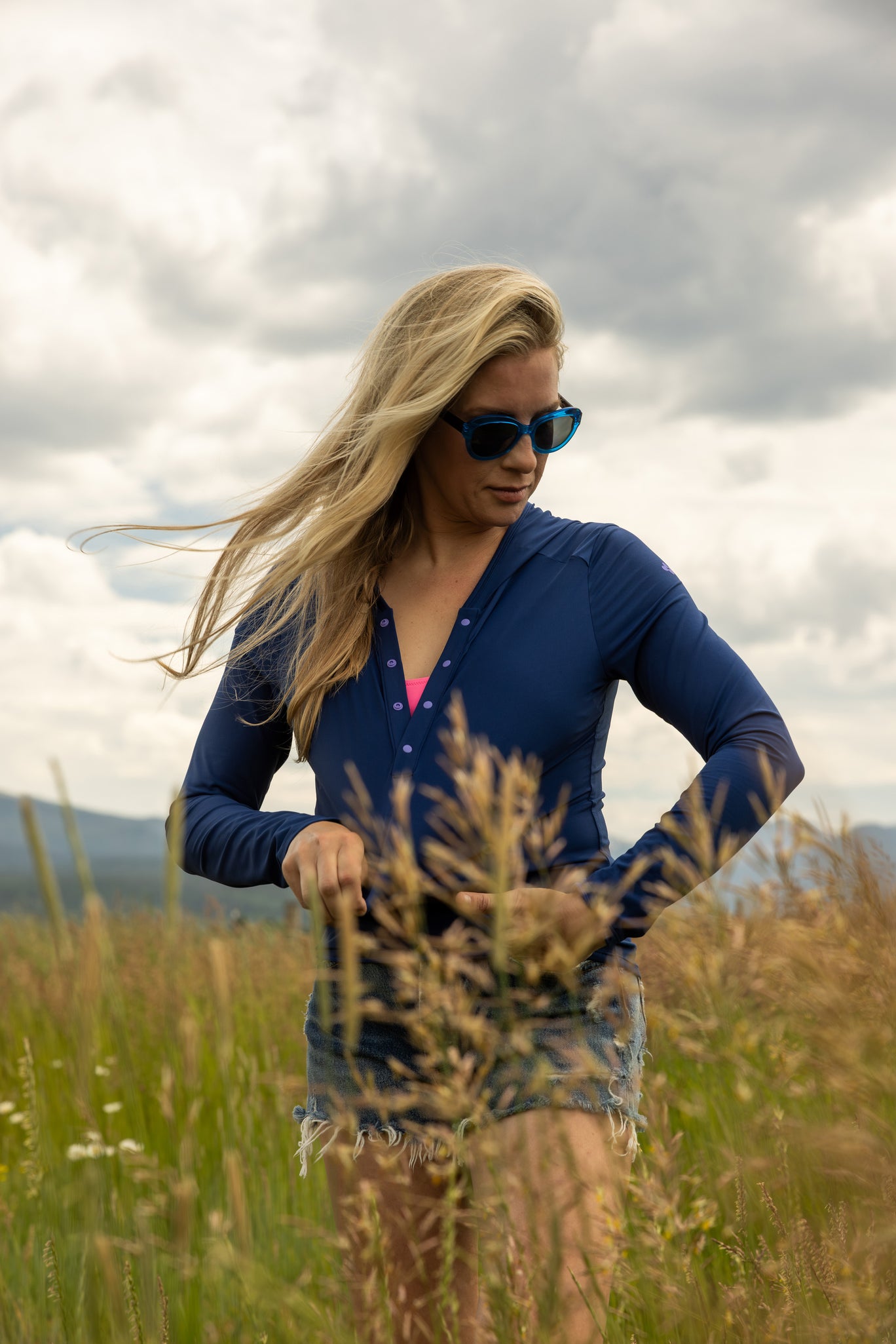 Woman in a blue sun shirt standing in a field with a cloudy sky.
