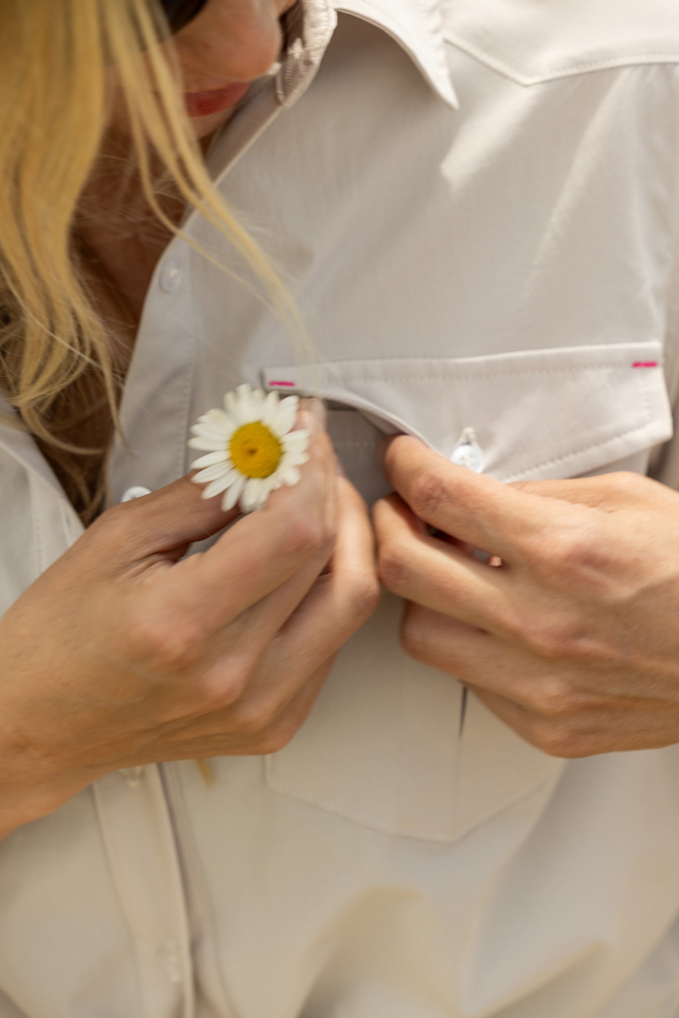 Woman attaching a white flower to a beige button down fishing shirt